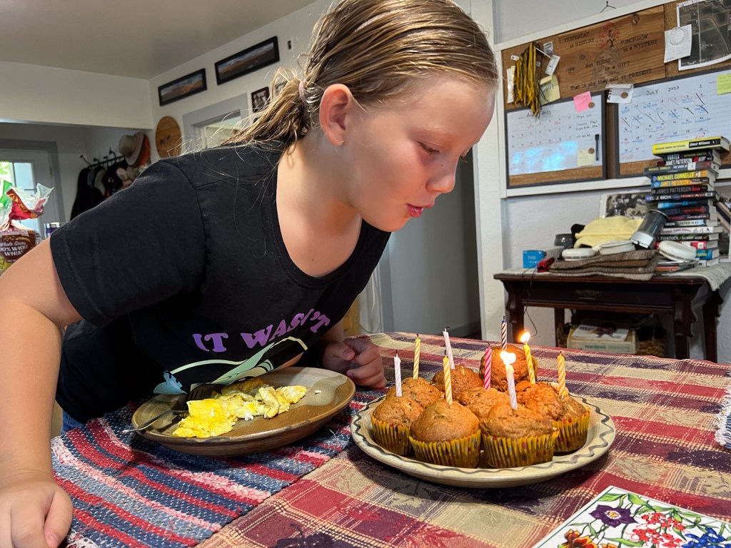 Girl blowing out birthday candles on muffins.