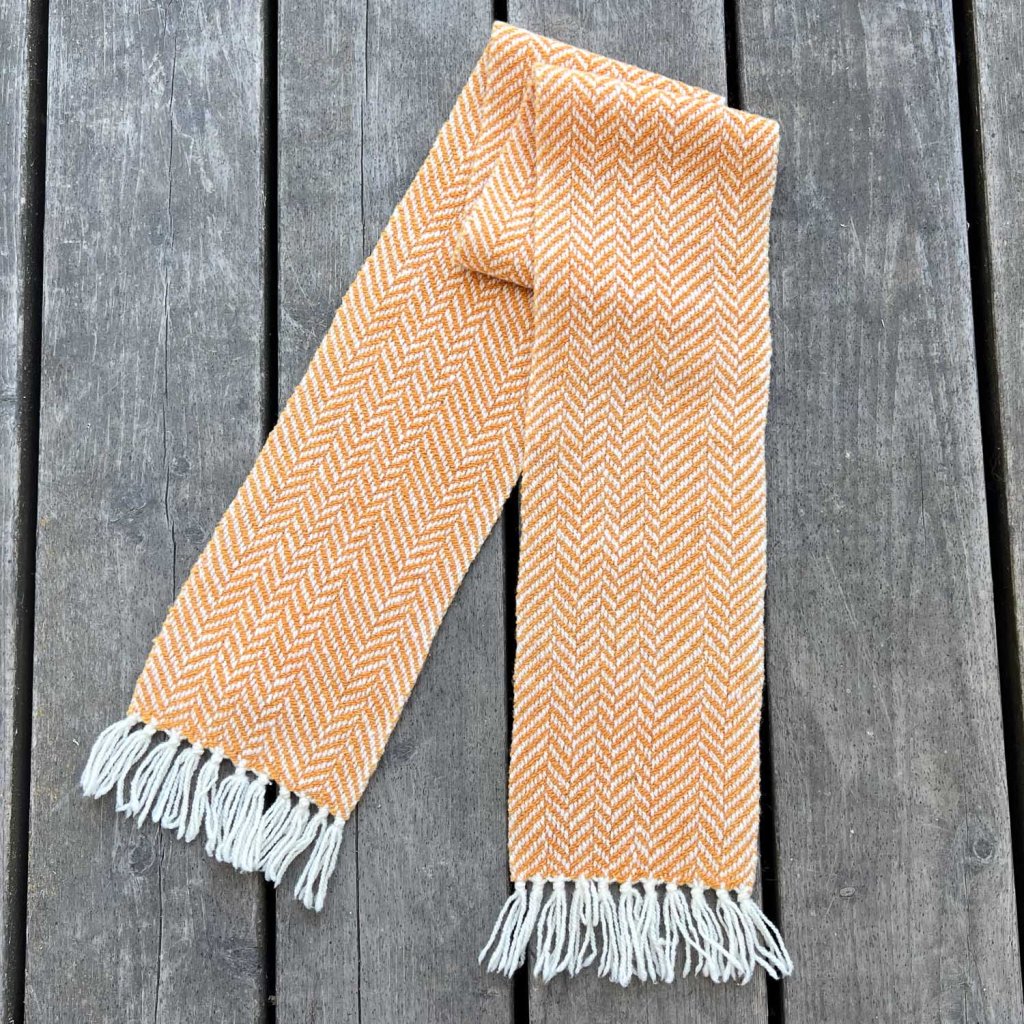 Orange herringbone patterned scarf on wood deck.
