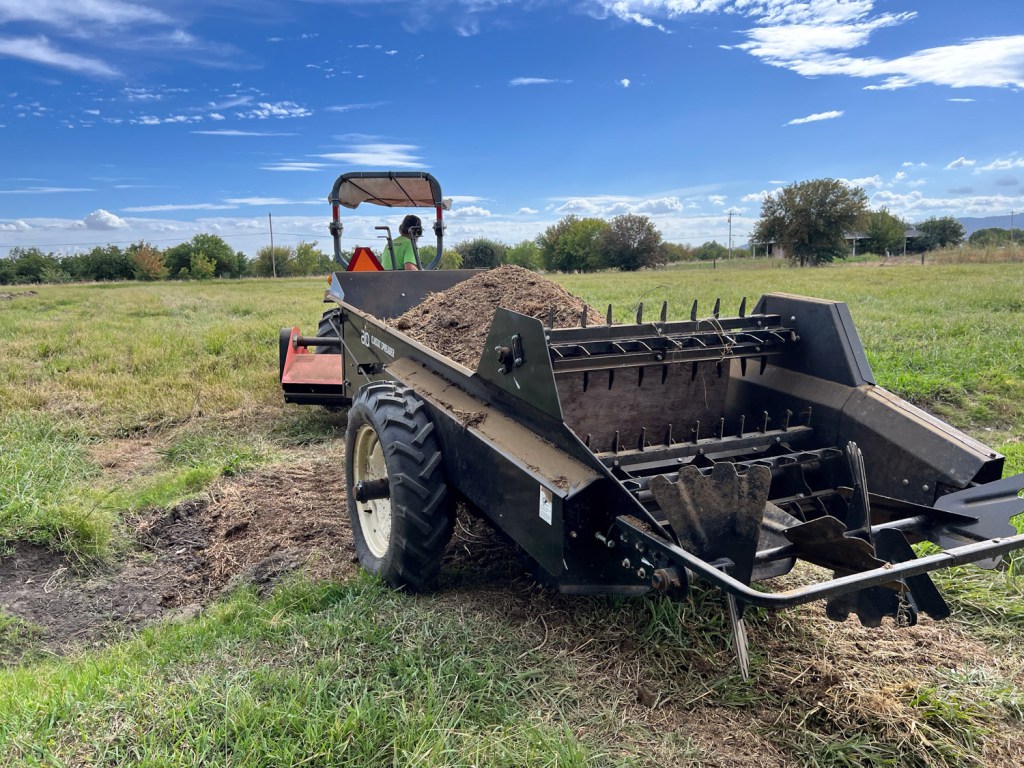 Manure spreader driving into green field.