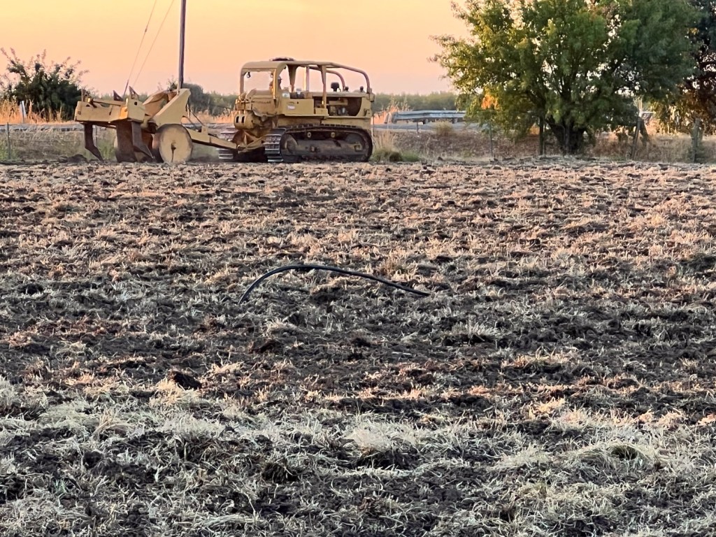 Early morning view of tractor with ripper behind it in dirt field.