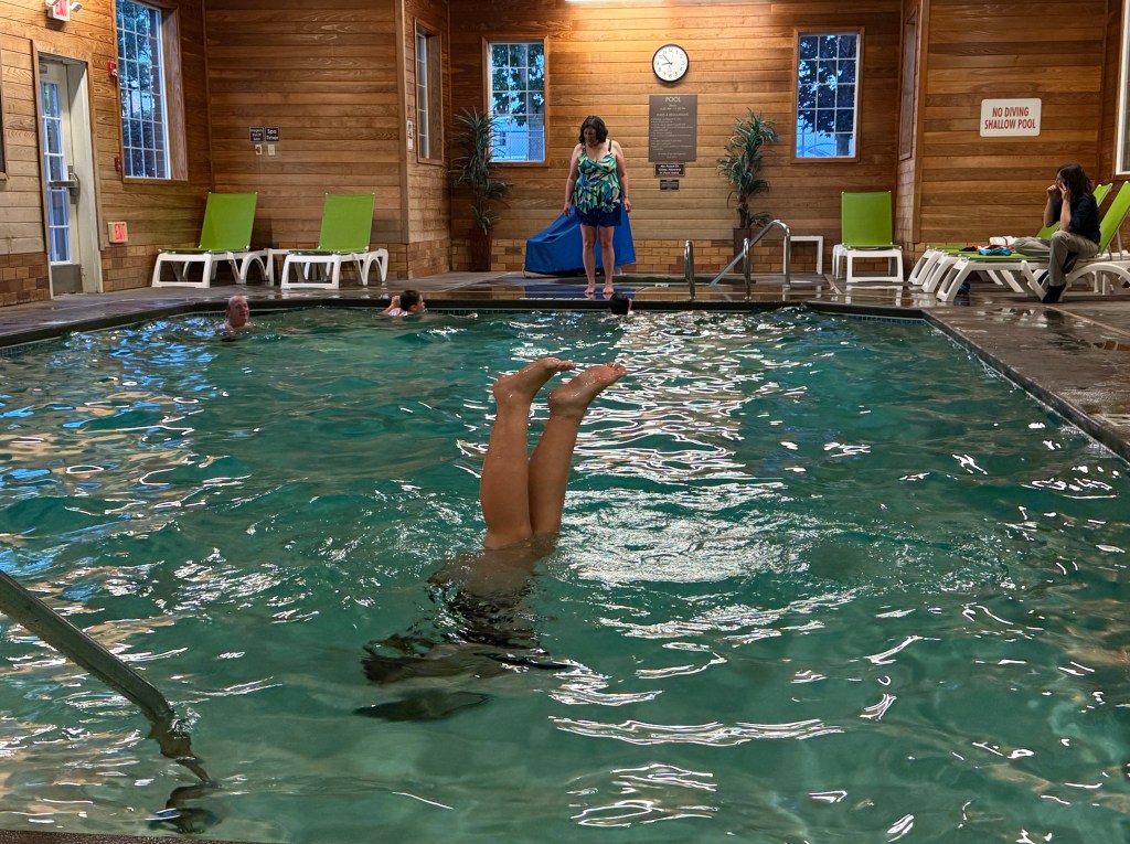 Girl doing handstand in swimming pool with only legs showing above the water.
