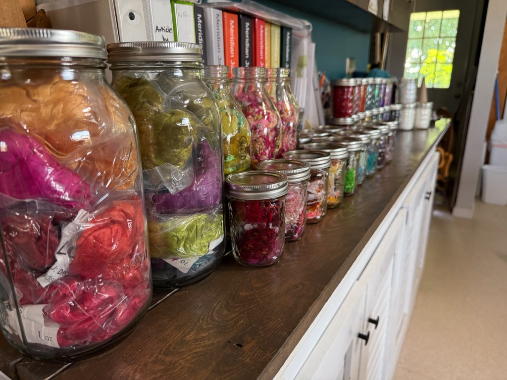 Glass jars full of colorful fiber on a shelf.