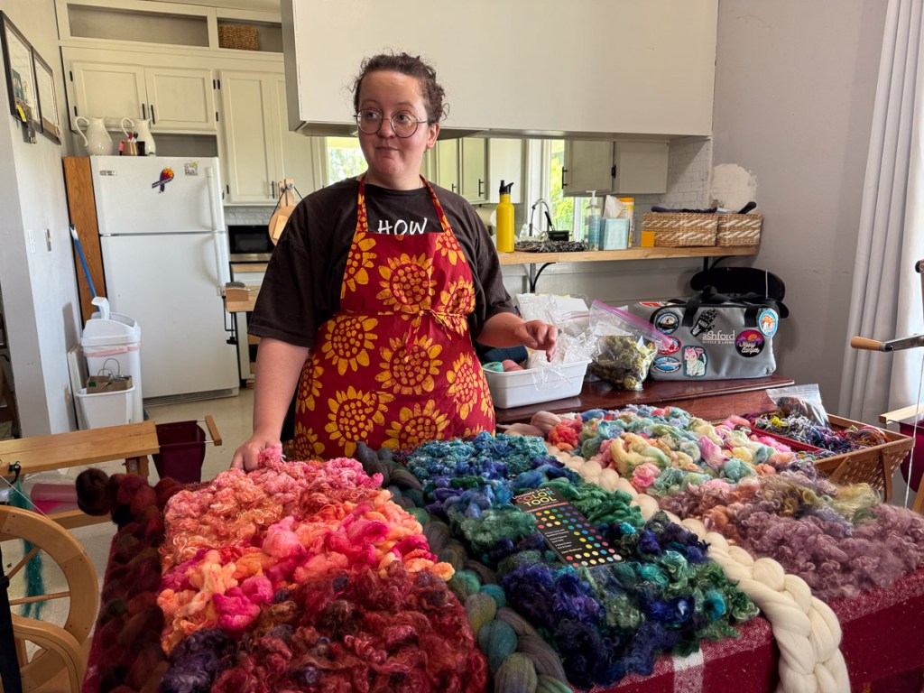 Teacher Rachel behind a table full of colorful fiber.