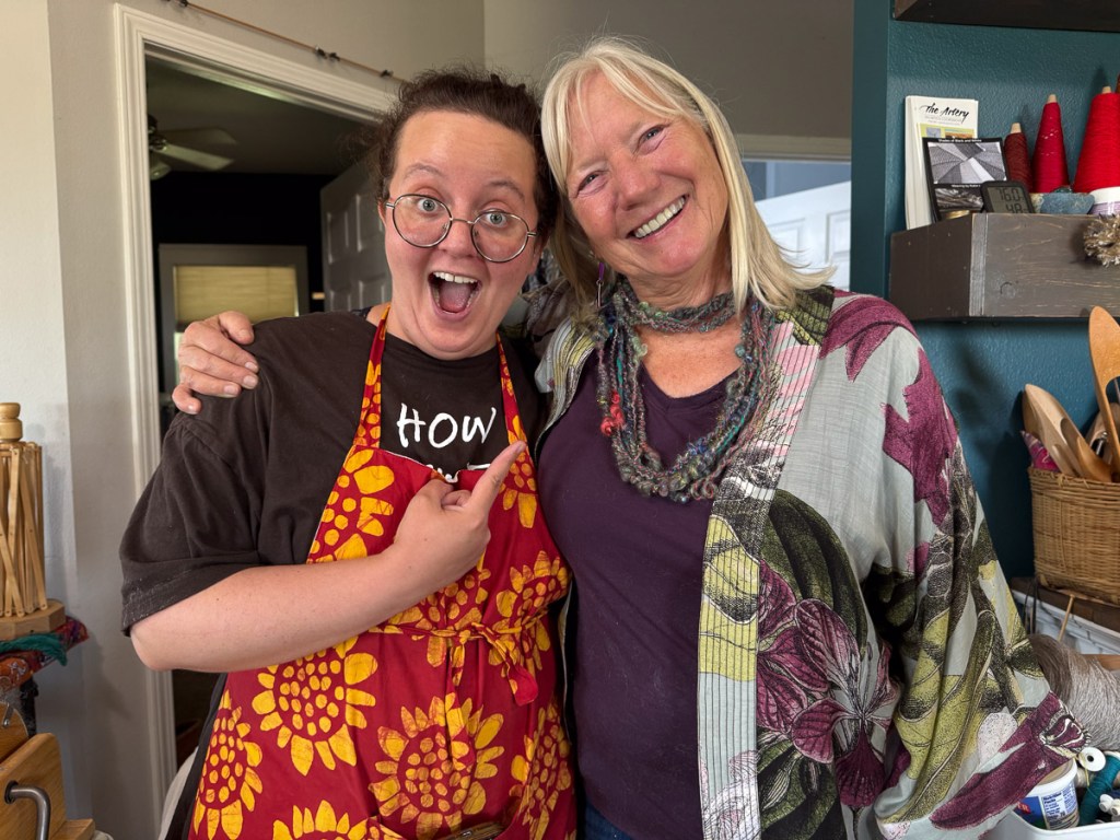 Two women, one wearing corespun yarn as a necklace, and the other expressing excitement over it.