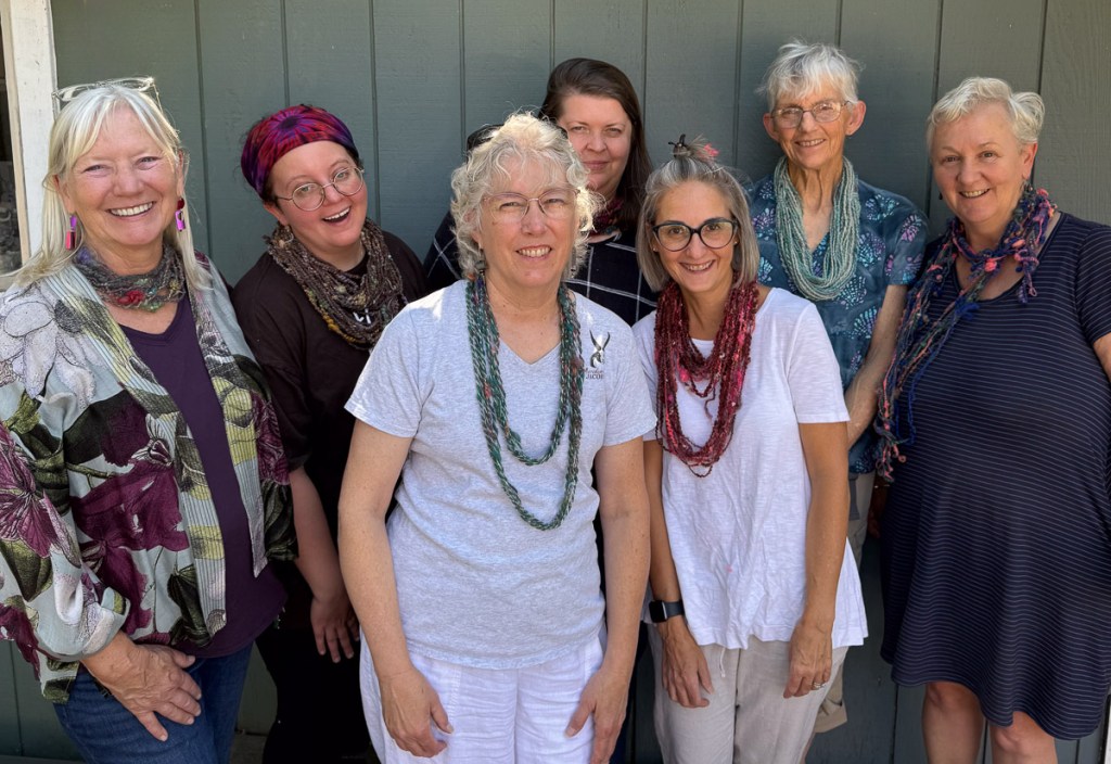 Seven women showing off the yarn they just spun after learning to core spin. Yarn is shown around the neck as a necklace. 