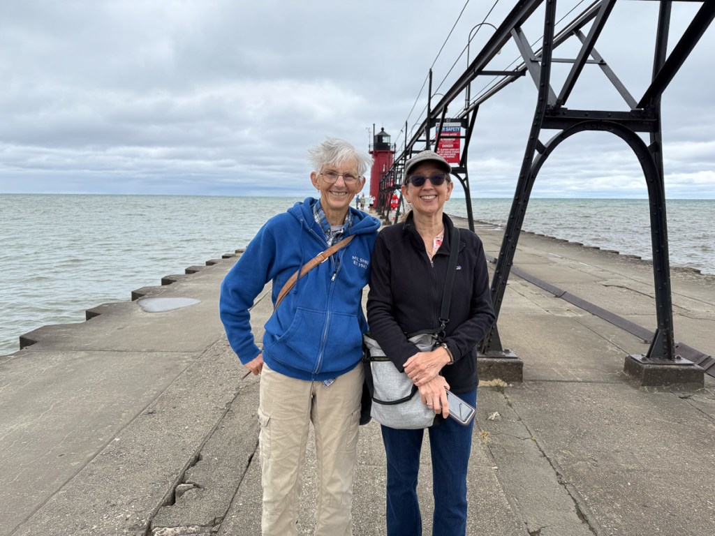 Two people on the pier into Lake Michigan with the lighthouse in the background.