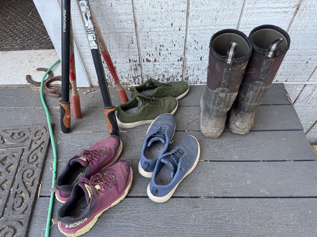 Three pairs of shoes in red, blue, and green with black rubber boots on a gray surface.