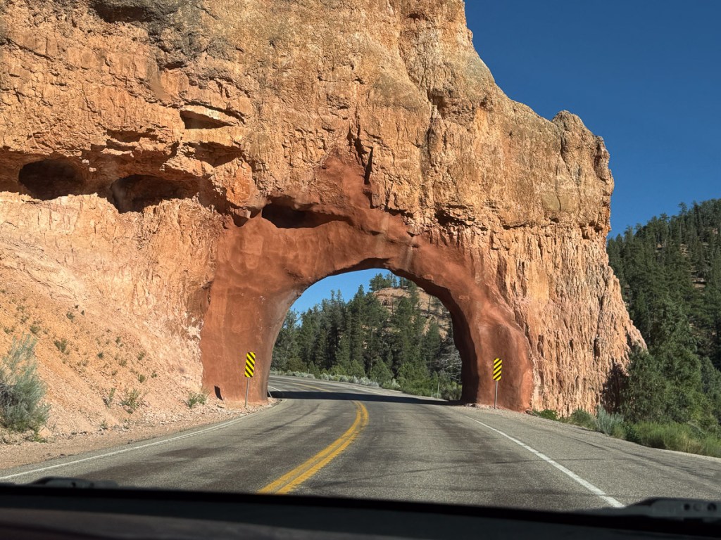 Two lane road that leads through a arch cut in the red rock in Utah.