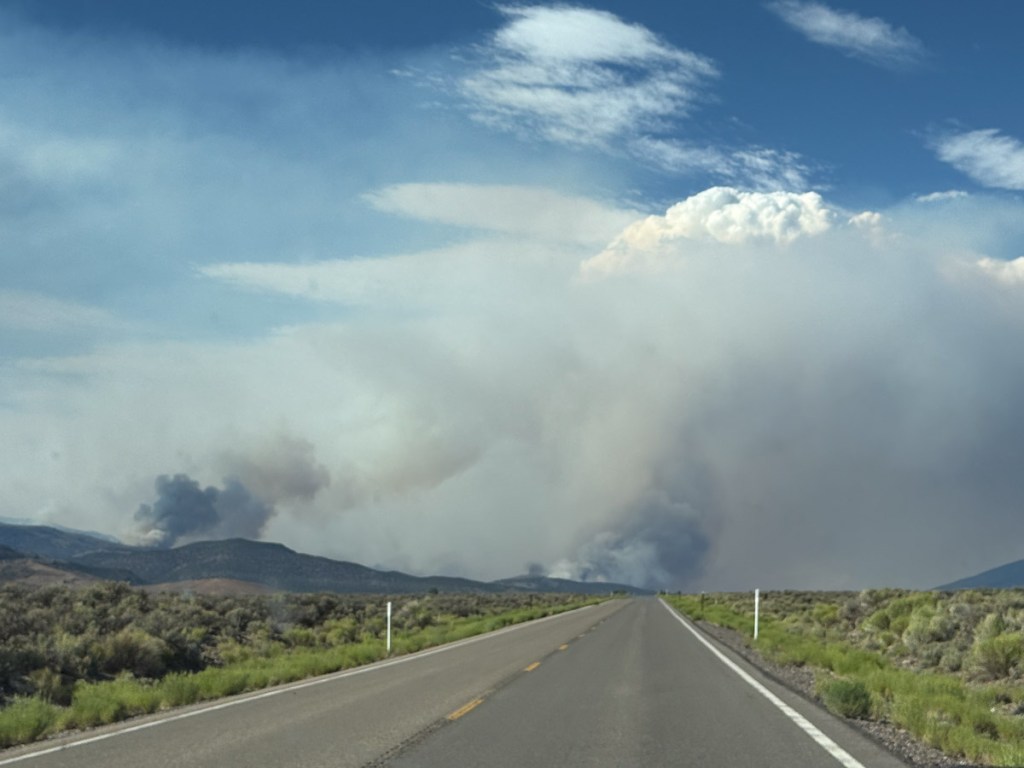 Smoke plumes over high desert landscape with road in the middle.