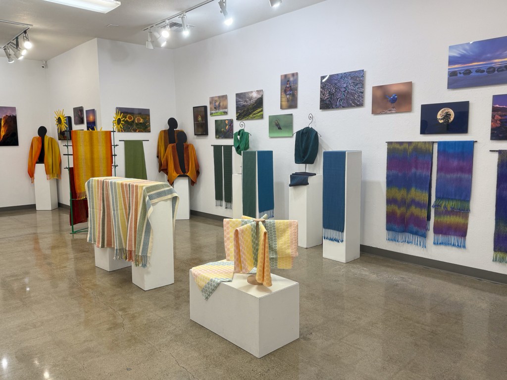 Woven pieces and photographs arranged by color in a gallery room.