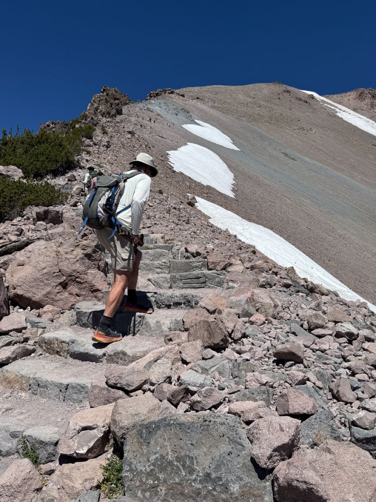 Dan hiking a trail off rocky stairs, heading toward the ridge. 