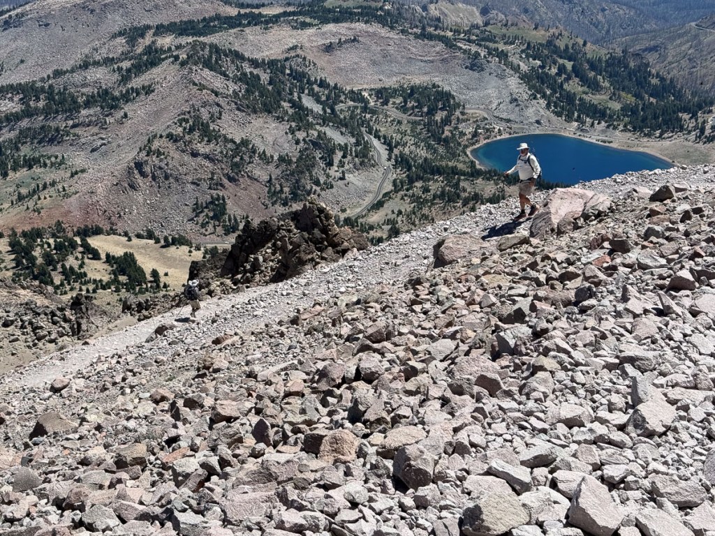 Hiker on rocky trail with view of landscape and blue lake in background.