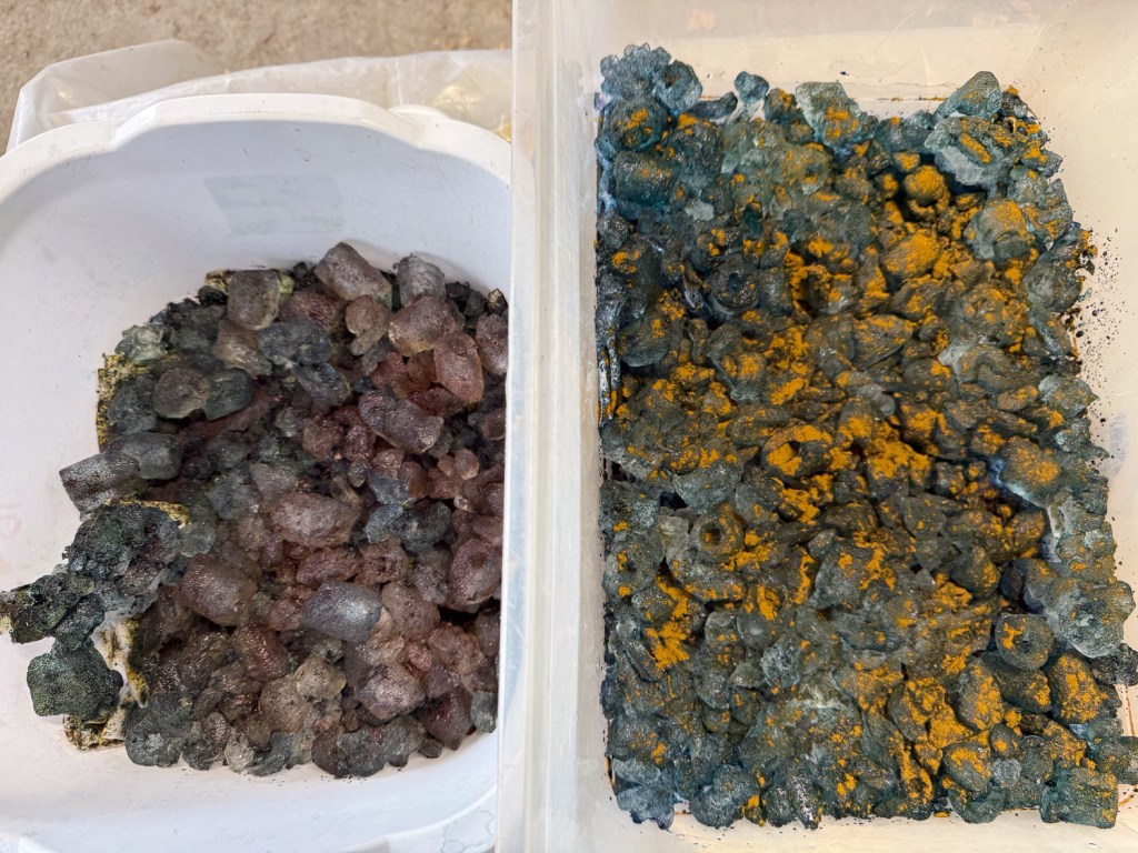 Two plastic tubs that hold fabric covered with ice and dye powder.