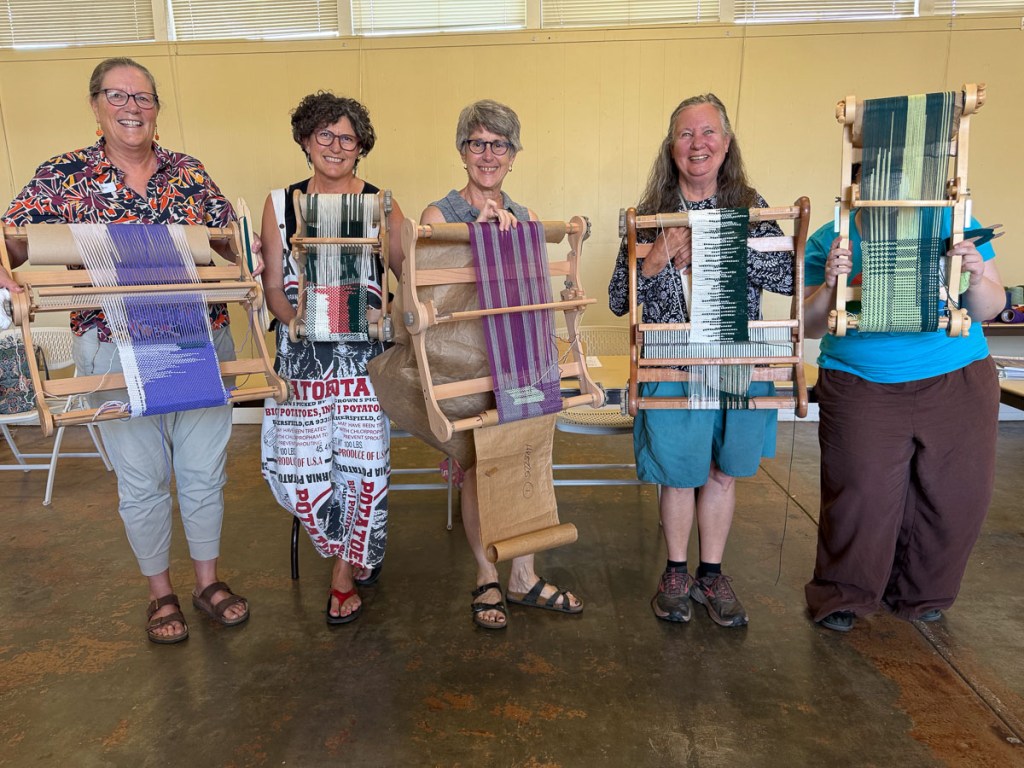 Five women holding looms with clasped warp projects they are working on in a class.