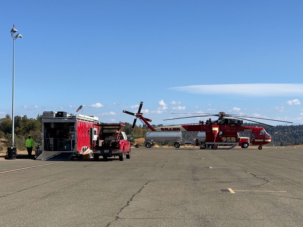 Sky-crane helicopter with its service vehicles nearby.